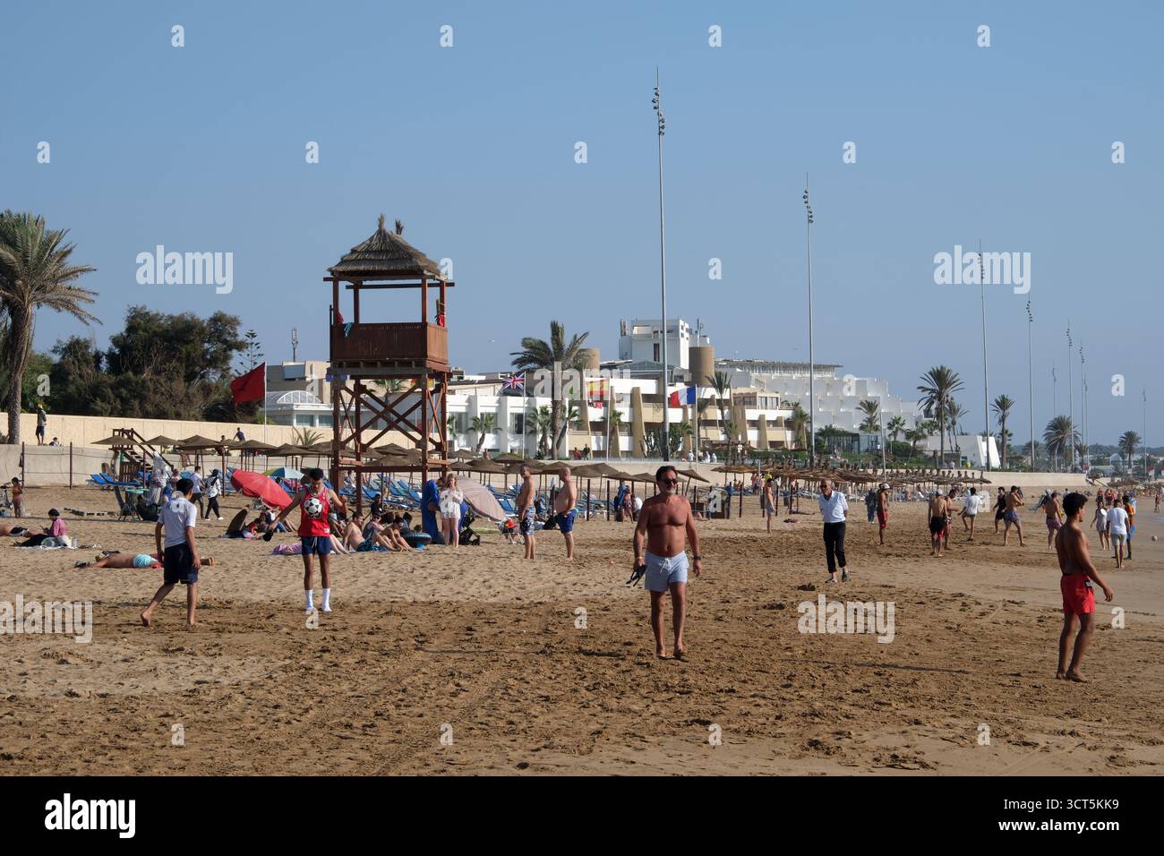 Hotels säumen den Strand und junge Männer spielen Fußball am Strand von Agadir, Marokko, Nordafrika Stockfoto