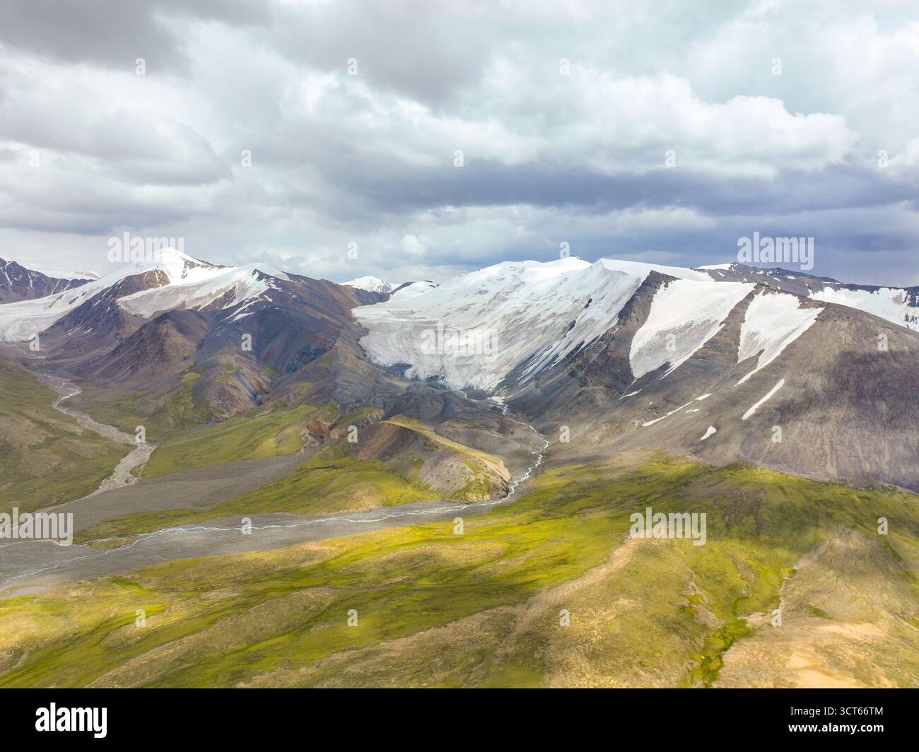 Weite Luftaufnahme eines Gebirges mit ausgedehnten Schneefeldern und Gletschern, die ein System von Schmelzwasserflüssen im Vordergrund speisen Stockfoto