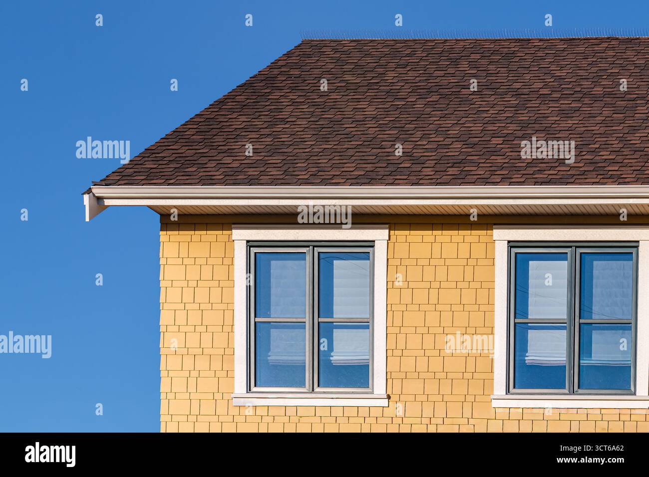 Top-Fassade eines traditionellen farbenfrohen Hauses. Gemustertes Ziegeldach auf gelbem Wohnhaus mit zwei Fenstern. Modernes Einfamilienhaus mit Fenstern. ph-wert der Reise Stockfoto