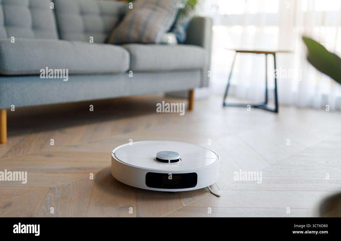 Weißer Roboter-Staubsauger auf Holzboden. Intelligente Reinigungstechnologie Stockfoto