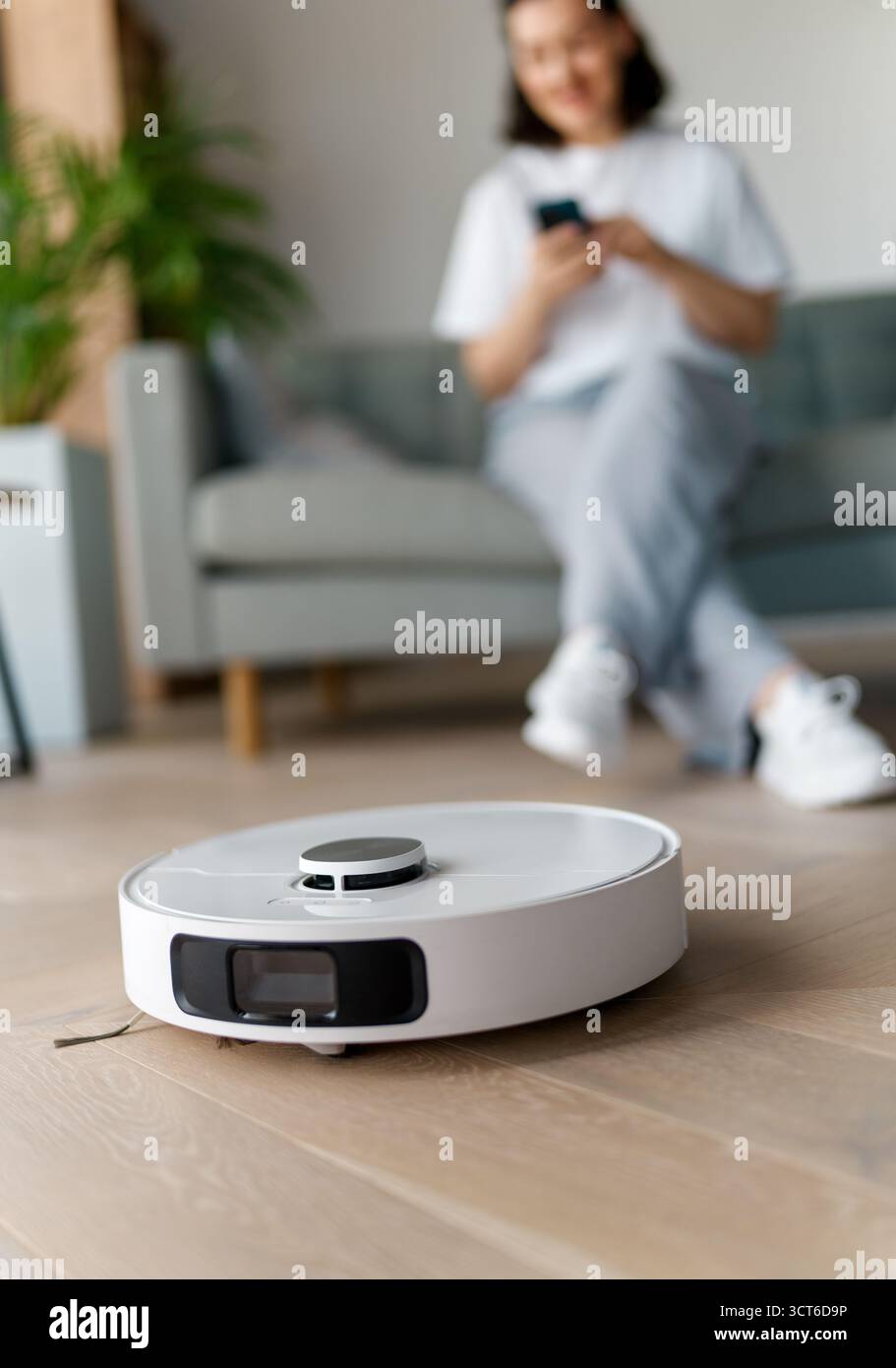 Weißer Roboter-Staubsauger auf Holzboden. Intelligente Reinigungstechnologie Stockfoto