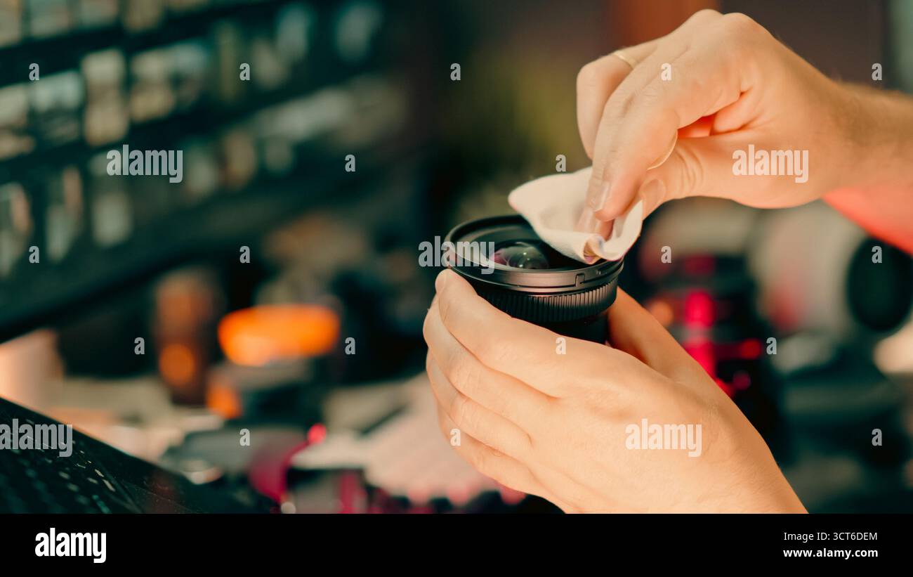 Reinigung der Kameraobjektive Wartung der Hände des Fotografen. Nahaufnahme eines Mannes, der das DSLR-Objektiv mit Mikrofasertuch am Schreibtisch in einem modernen Kreativstudio reinigt, Profe Stockfoto