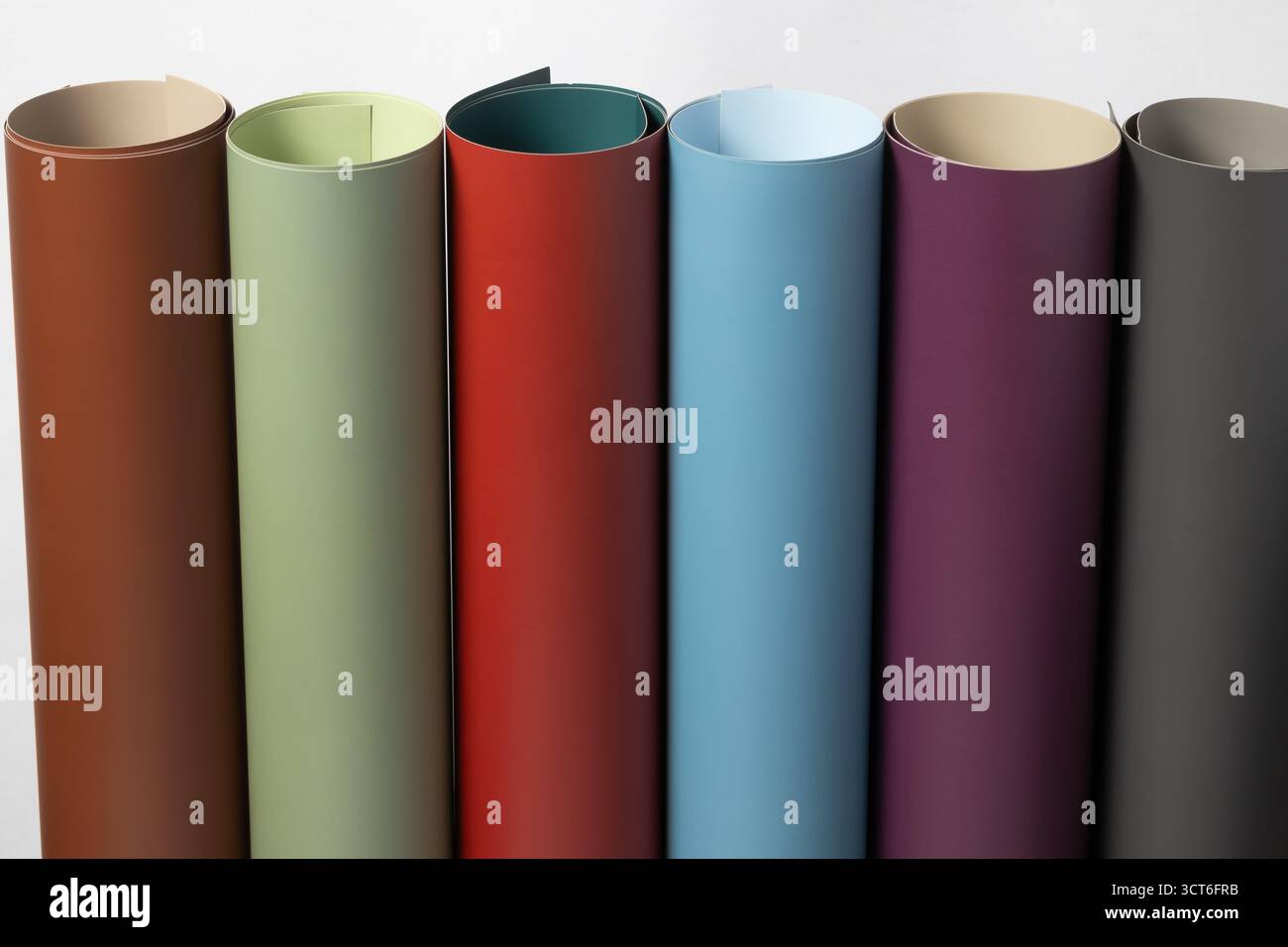 Eine Reihe von bunten, gerollten Materialien, wie Papier oder Kunstleder, in kräftigen Tönen: Braun, Salbei, Rot, Petrol, Aubergine, und anthrazitgrau Stockfoto