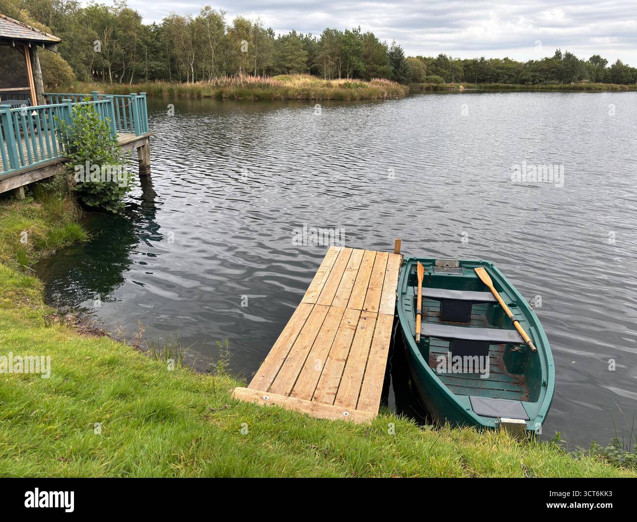Angelschleuse und Pier mit verankertem Boot auf dem See in Schottlands Grenzregion mit Holzsteg, Schiffsrumpf, Wasseroberfläche und fernem Moor Stockfoto