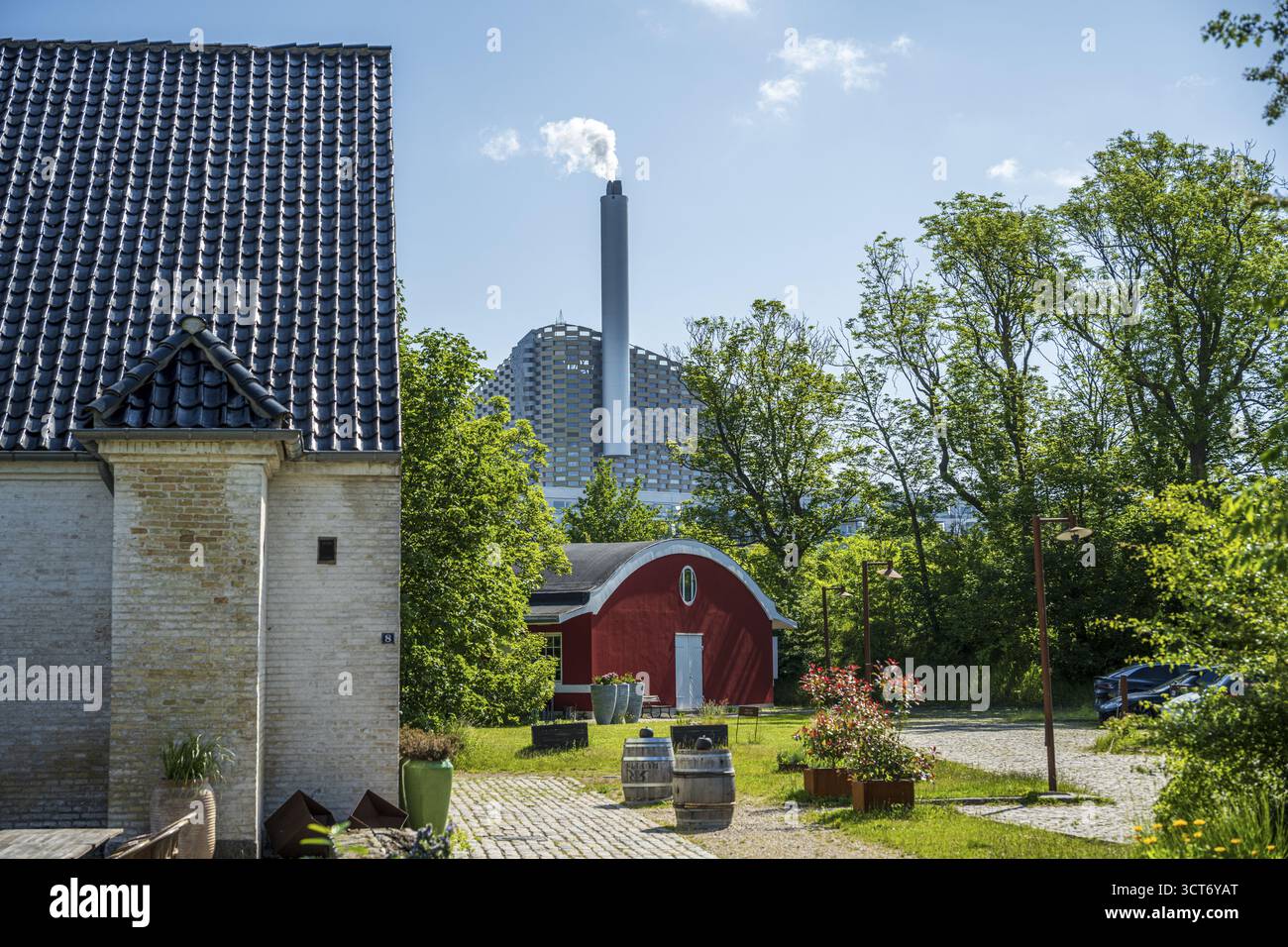 Ziegelgebäude vor grünem Hintergrund mit einem sichtbaren Kamin im Hintergrund, aus dem Rauch steigt, Abfallverbrennungsanlage, Copenhill, Co Stockfoto