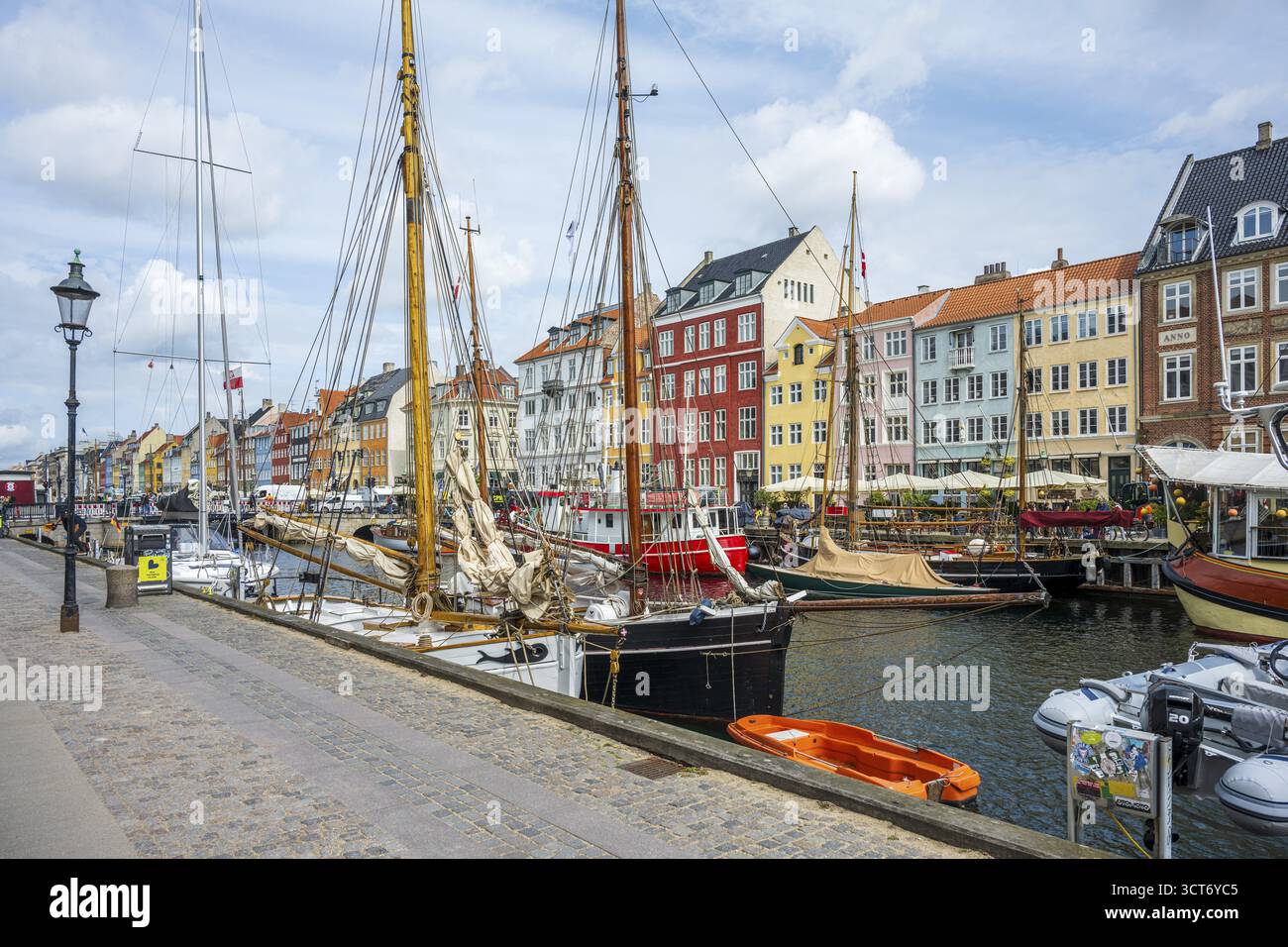 Stadthafen mit Holzbooten, farbenfrohen Gebäuden und bewölktem Himmel entlang eines Kopfsteinpflasterpfads, Nyhavn, Kopenhagen, Dänemark Stockfoto