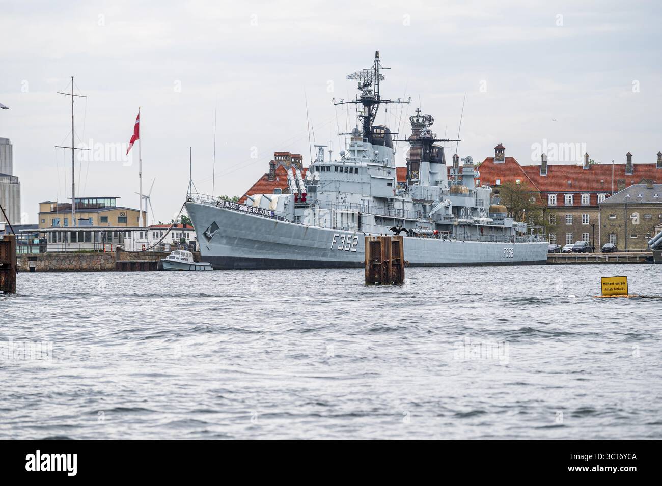 Graues Kriegsschiff im Hafen vor roten Ziegeldächern unter bewölktem Himmel, Hafen, Kopenhagen, Dänemark Stockfoto