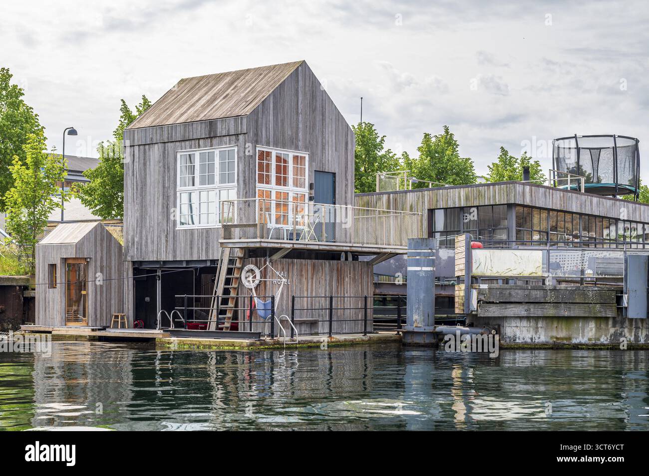 Ein minimalistisches Holzhaus mit Terrasse und Treppen an einem Kanal, umgeben von Grün, Tiny Hotel, Kopenhagen, Dänemark Stockfoto