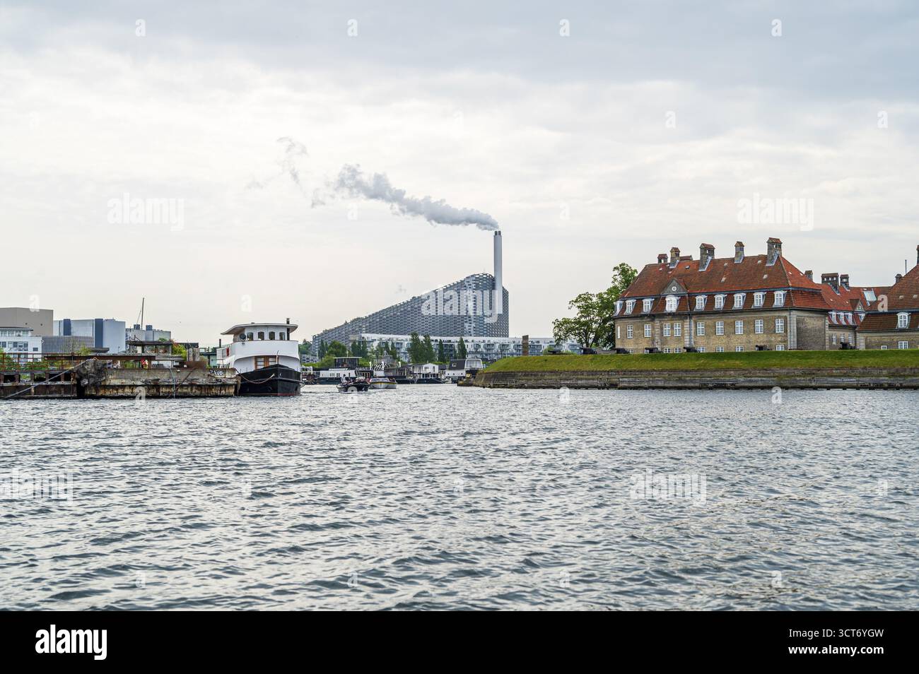 Wasserstraße mit Rauchschornstein im Hintergrund, flankiert von Gebäuden mit roten Dächern, Abfallverbrennungsanlage, Copenhill, Kopenhagen, Dänemark Stockfoto