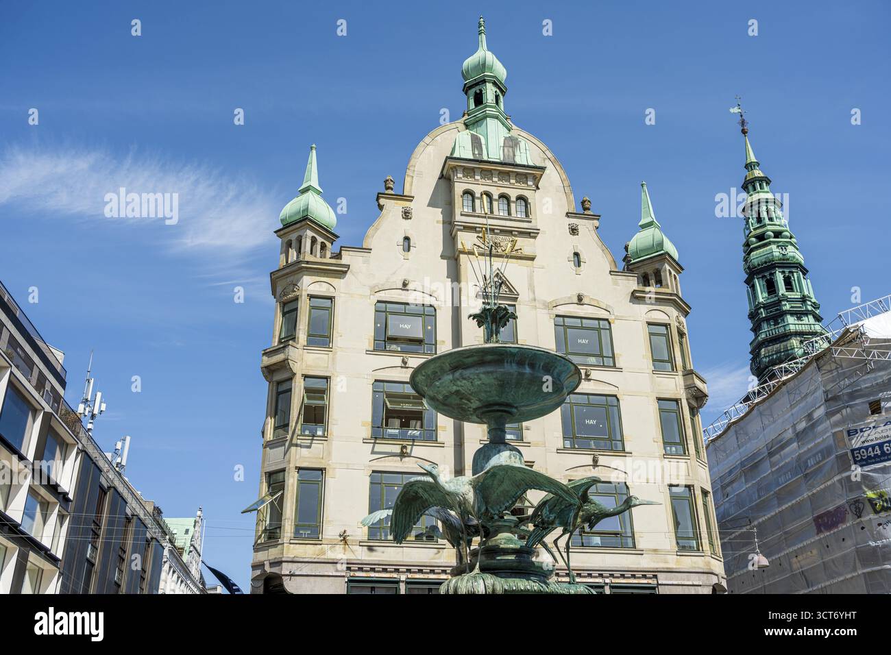 Historischer Brunnen vor einem Gebäude mit Türmen unter blauem Himmel, Storchbrunnen, Kopenhagen, Dänemark Stockfoto