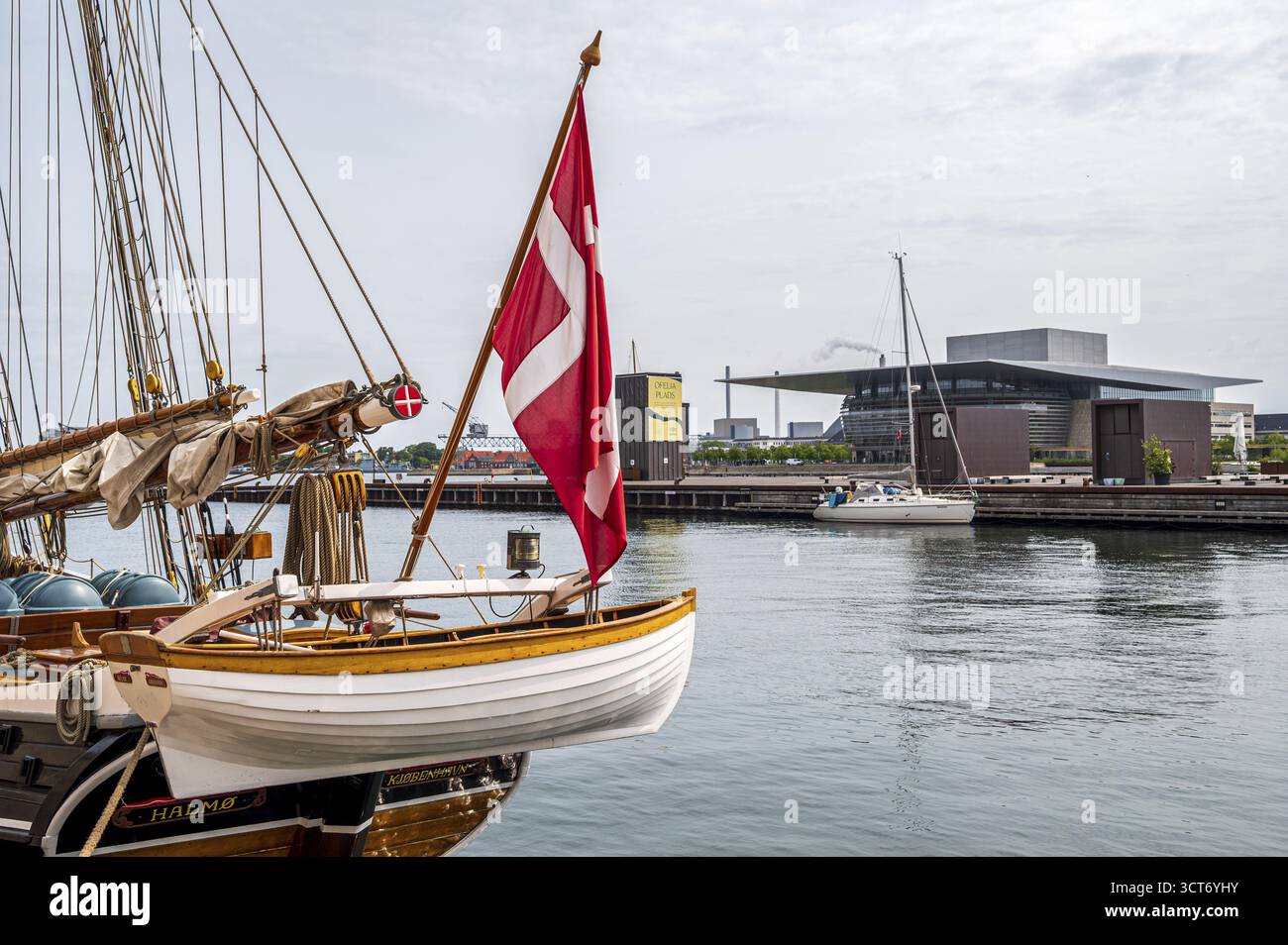 Ein Segelboot unter dänischer Flagge, das im Hafen mit Blick auf das Opernhaus in Kopenhagen, Kopenhagen, Dänemark, vor Anker liegt Stockfoto