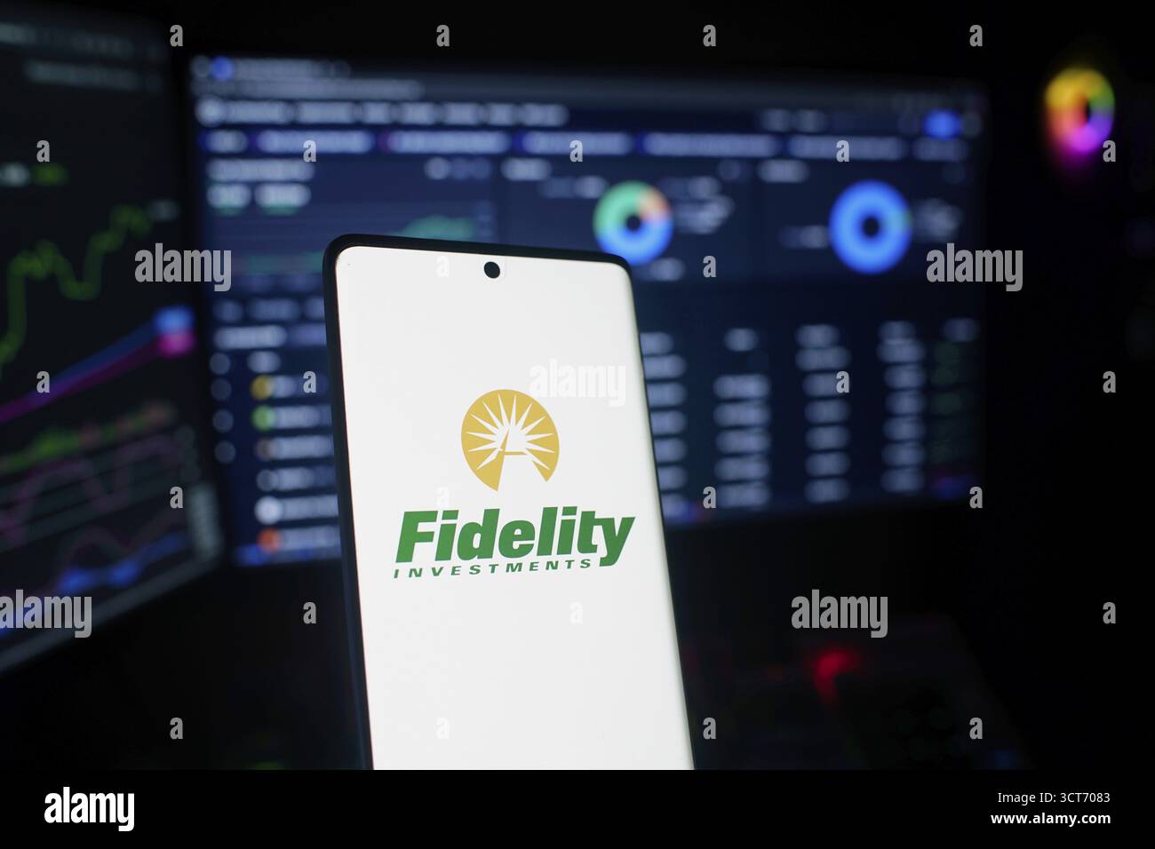 Smartphone mit Fidelity Investments Logo und Handelsbildschirmen im Hintergrund Stockfoto