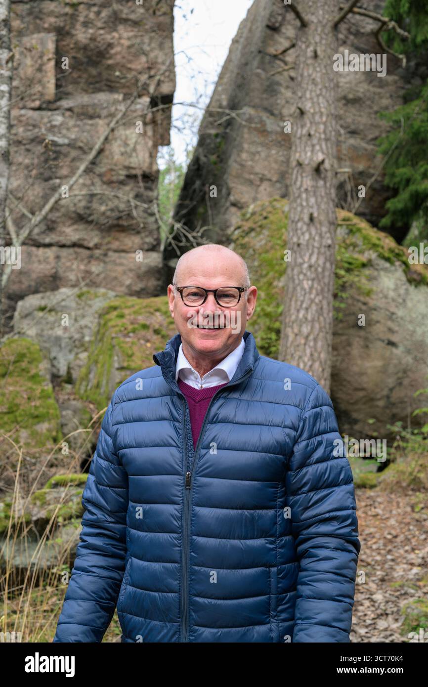 Porträt eines älteren Mannes, der in den Wäldern lächelt, mit Felsformation im Wald Nordeuropas Stockfoto
