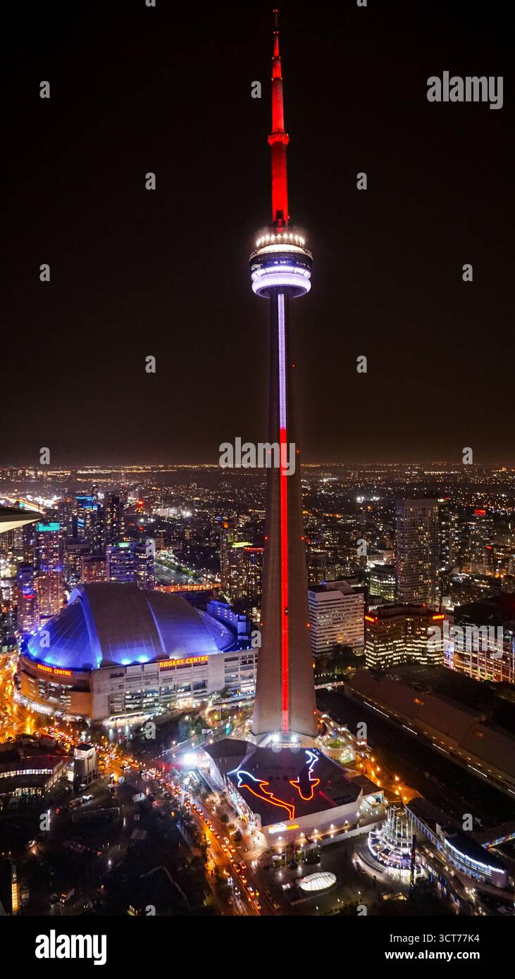 Nächtlicher Blick auf den CN Tower, beleuchtet in roten und weißen Lichtern, mit Blick auf die Innenstadt von Toronto mit dem Rogers Centre, das in Blau leuchtet. Stockfoto