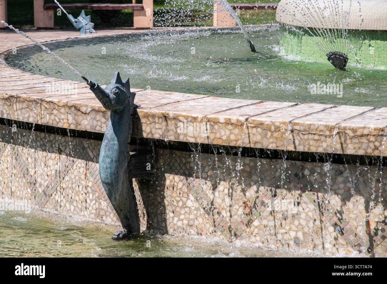 Eine kupferne Fischskulptur in einem städtischen Wasserbrunnen mit plätscherndem Wasser an einem sonnigen Tag Stockfoto
