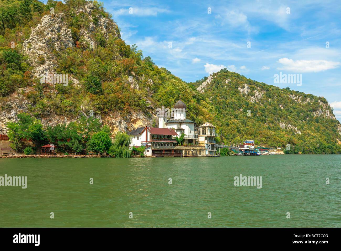 Das Kloster Mraconia liegt am Fuße einer hoch aufragenden Klippe über der breiten Donau in Rumänien, mit Booten, die entlang der felsigen Küste und der dramatischen schlucht vertäut sind Stockfoto