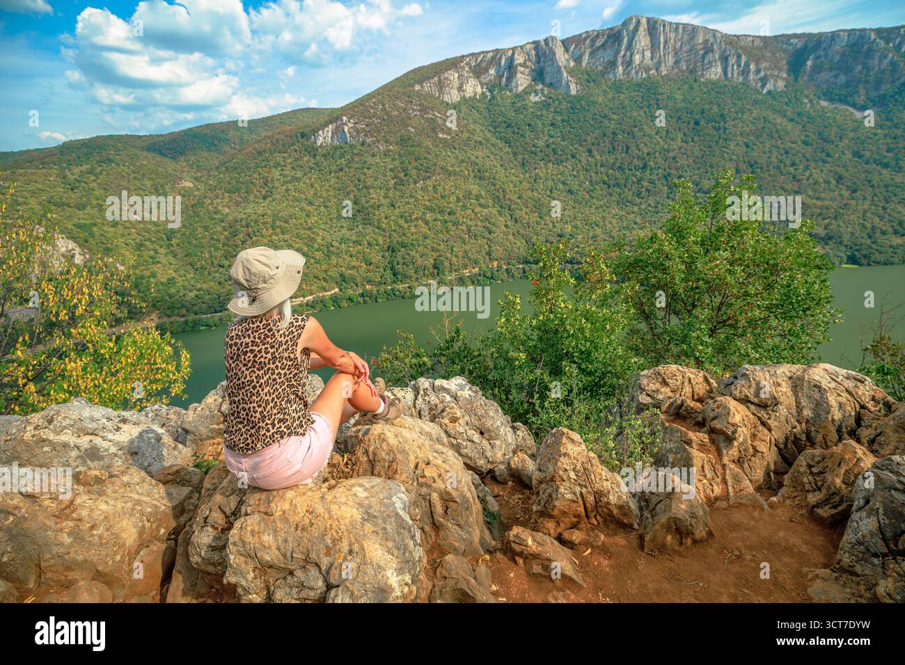Frau sitzt auf Felsen und genießt den weiten Panoramablick auf die Donauschlucht und die bewaldeten Berge im Djerdap Nationalpark Stockfoto