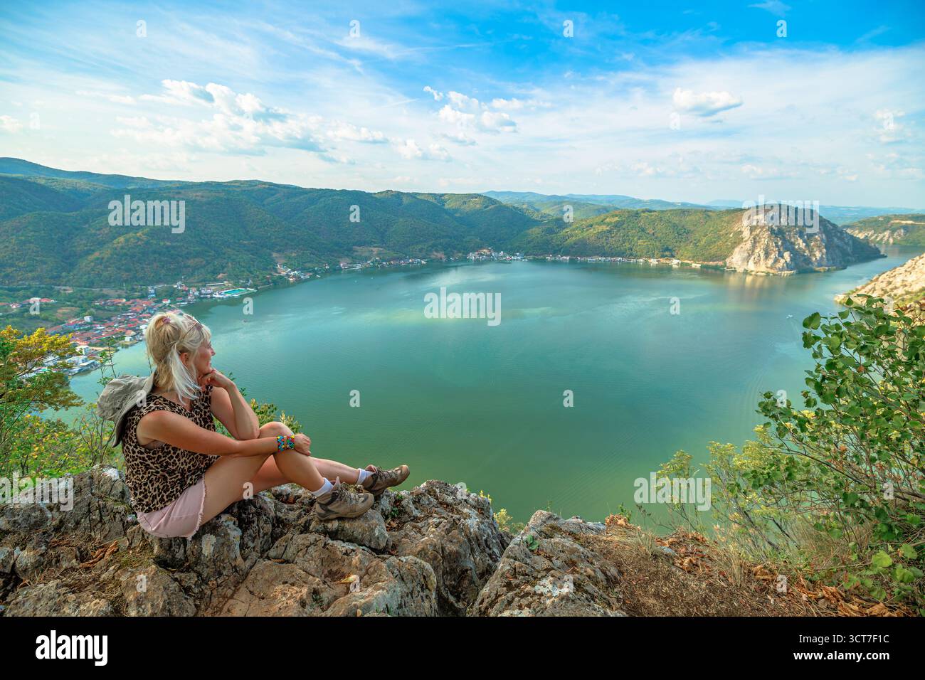 Frau sitzt auf Felsen und genießt den weiten Panoramablick auf die Donauschlucht in Rumänien und bewaldete Berge im Djerdap National Par Stockfoto