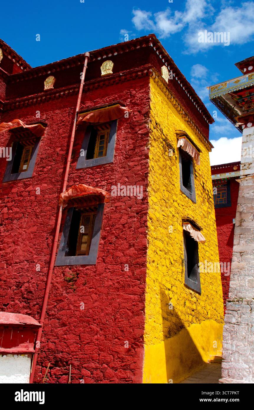 Lebendige Tibetische Klostermauer mit roten und gelben Texturen vor dem hellen blauen Himmel, die Details zum kulturellen Erbe und zur spirituellen Architektur zeigt. Stockfoto