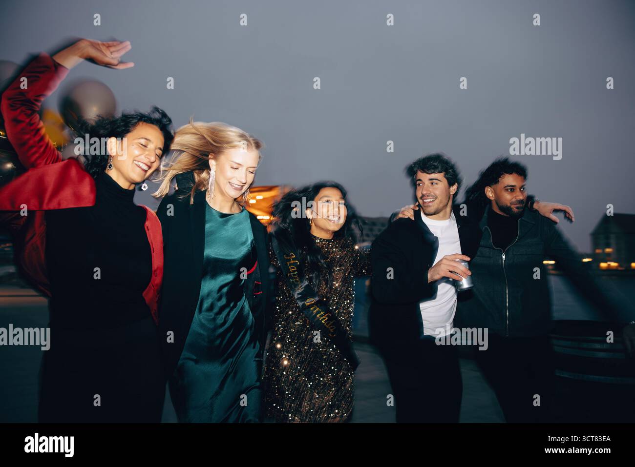 Fünf Freunde genießen sich abends im Freien, elegant gekleidet, lachen und verbinden sich, während sie gemeinsam feiern und eine fröhliche Atmosphäre schaffen Stockfoto