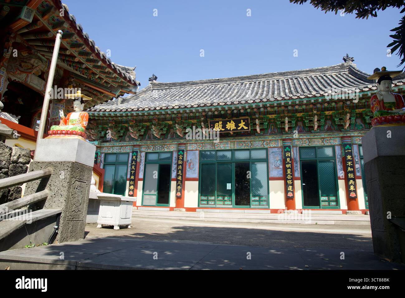 Farbenfrohe Schutzstatuen flankieren die Stufen in eine Haupthalle von Daeungjeon in der Nähe von Seongsan, mit Danceong-Mustern und gekachelten Traufen, die den ruhigen Courtya umrahmen Stockfoto