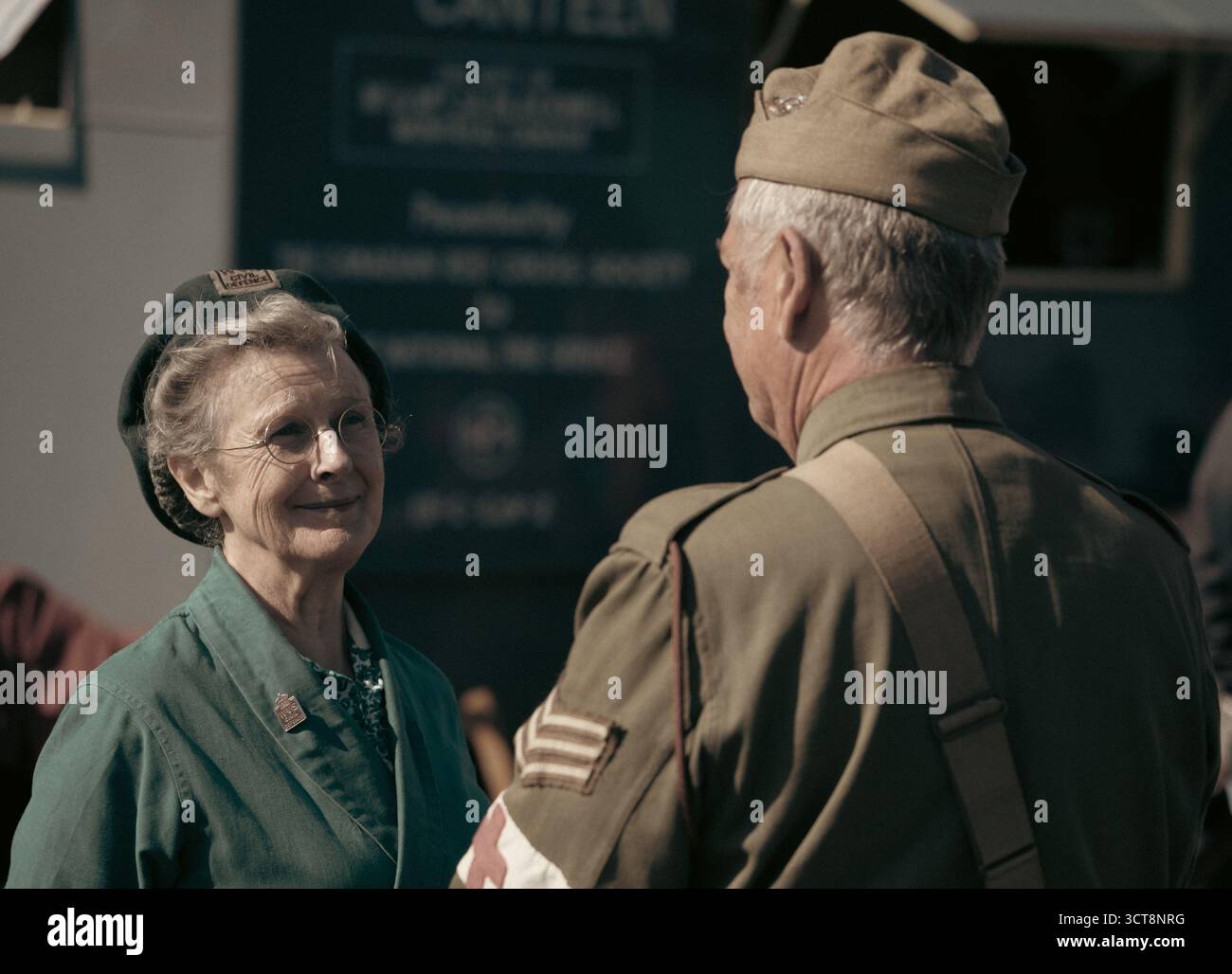 Ältere Frau im Kleid der 1940er Jahre, die mit einem Reenactor aus Kriegszeit in Militäruniform auf dem Heritage Event spricht Stockfoto