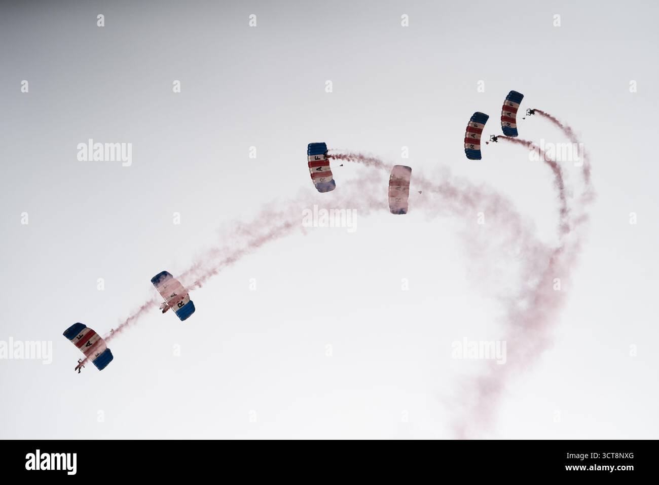 Das Fallschirmteam der RAF Falcons führt Flugmanöver mit roten Rauchspuren auf der Duxford Airshow durch Stockfoto