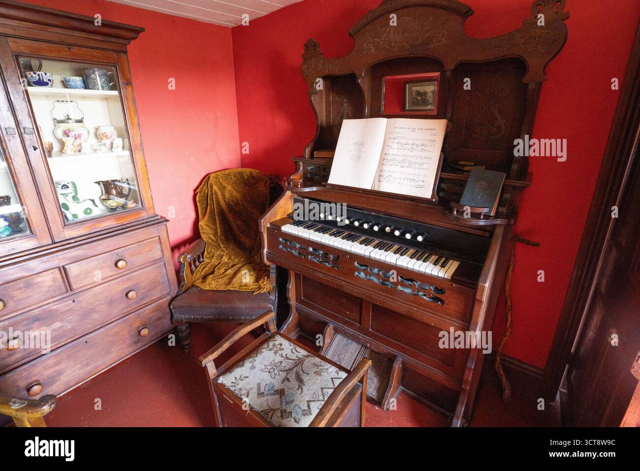 Viktorianisches Harmonium mit Noten in traditionellem, rot ummauertem Salon Stockfoto