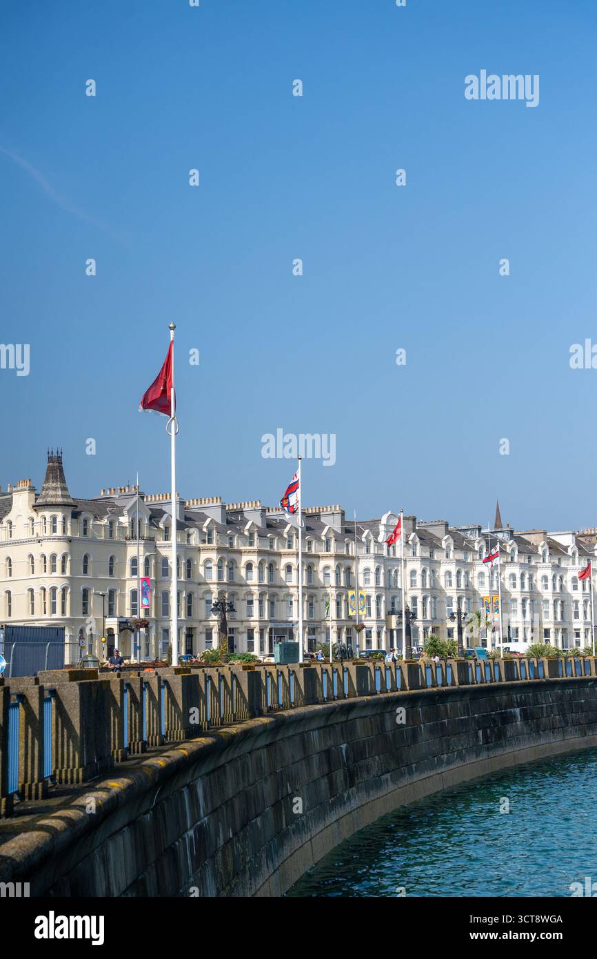 Viktorianische Strandpromenade mit Manx-Flaggen und Hotels mit weißen Terrassen unter blauem Himmel Stockfoto