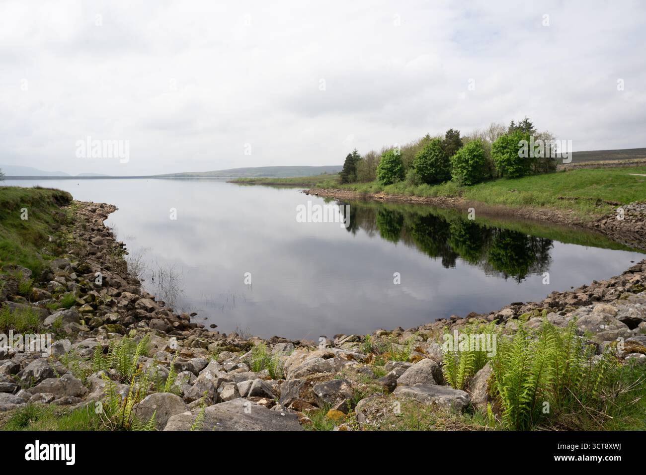 Ruhiger Stausee mit Steinküste und grünen Reflexen der Landschaft unter dem bewölkten Yorkshire-Himmel Stockfoto