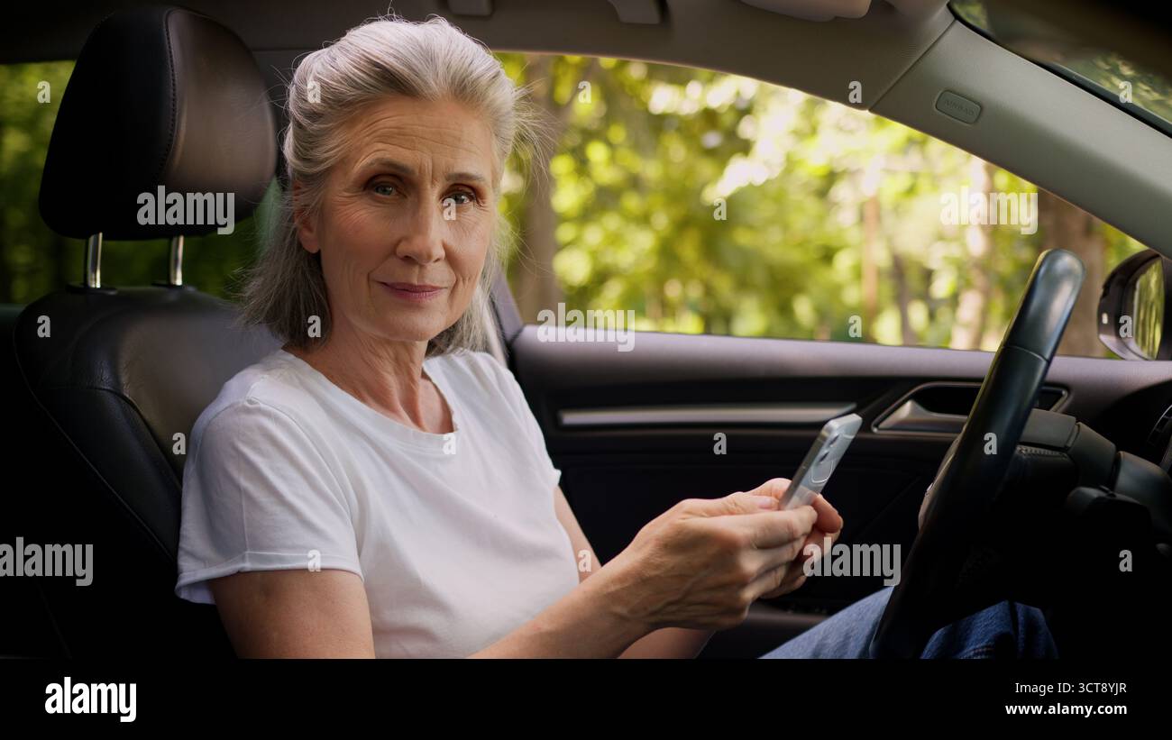 Fröhliche kaukasische reife Frau ältere ältere ältere Frau Rentner Auto Fahrer im Auto mit Handy spielen Spiel Ballen Faust Stockfoto