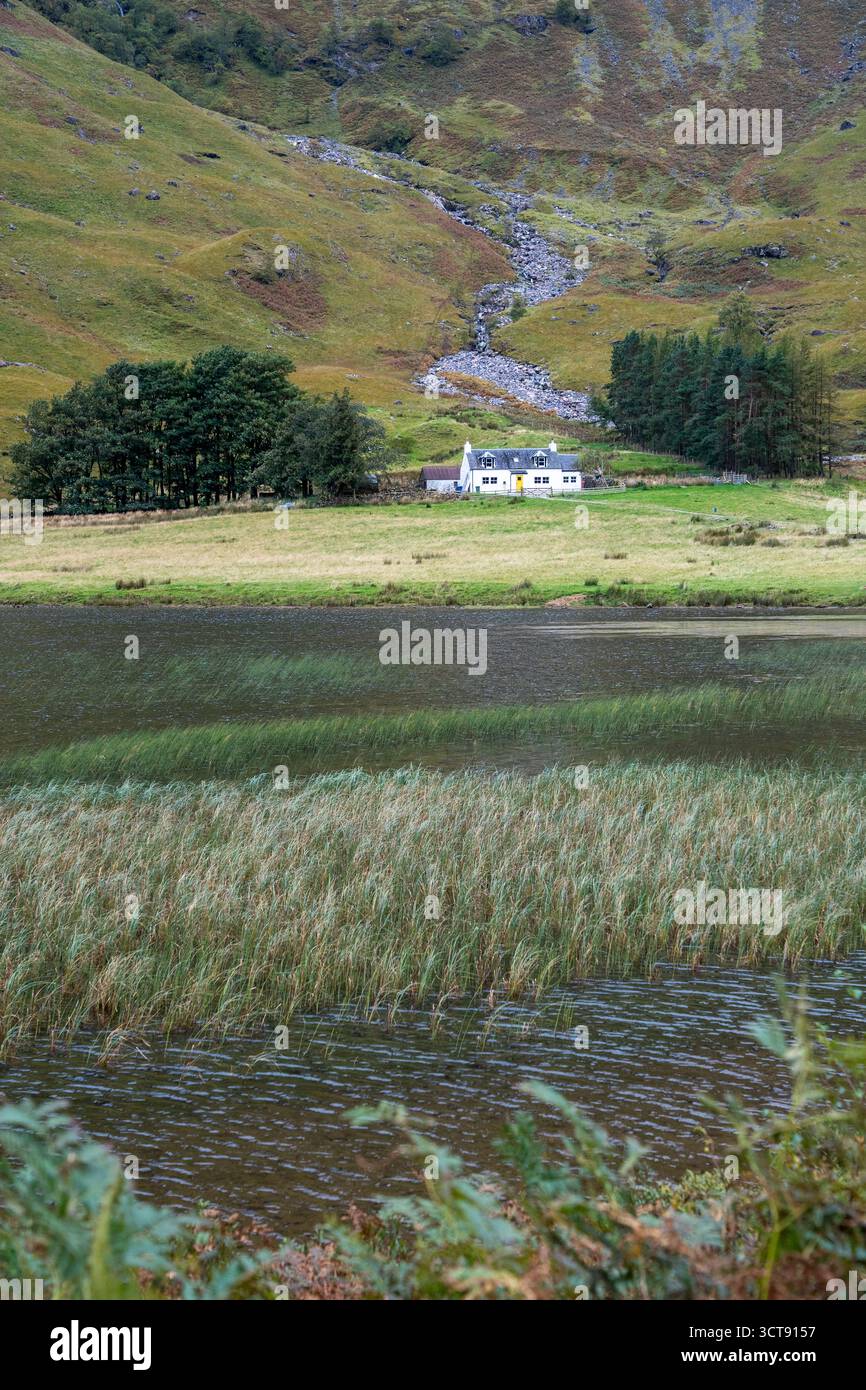 Abgelegene schottische Hütte neben Loch mit Bergbach und Herbstmoorland Stockfoto