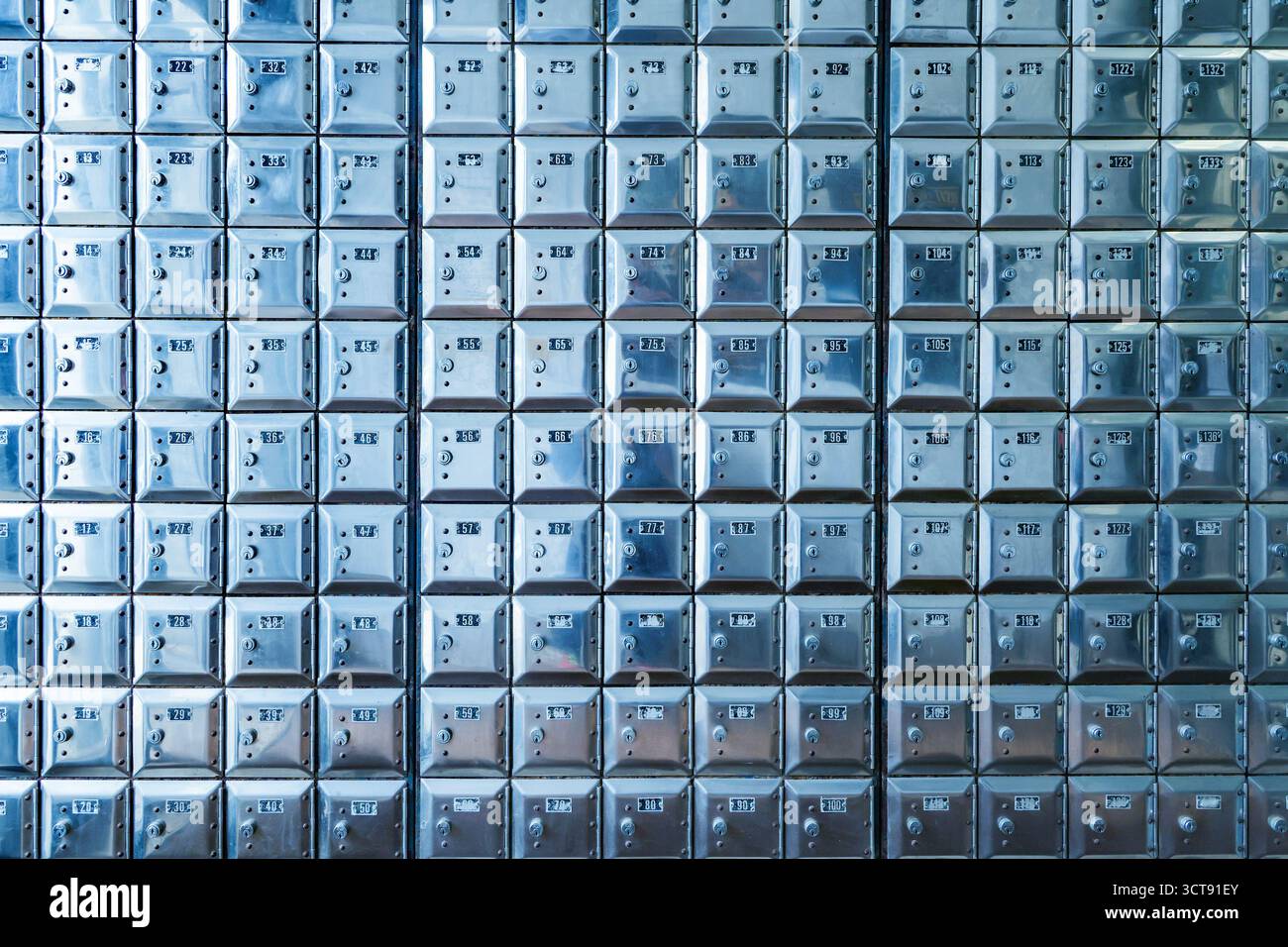 Die Wand ist voller Reihen alter, glänzender Metallkisten Stockfoto