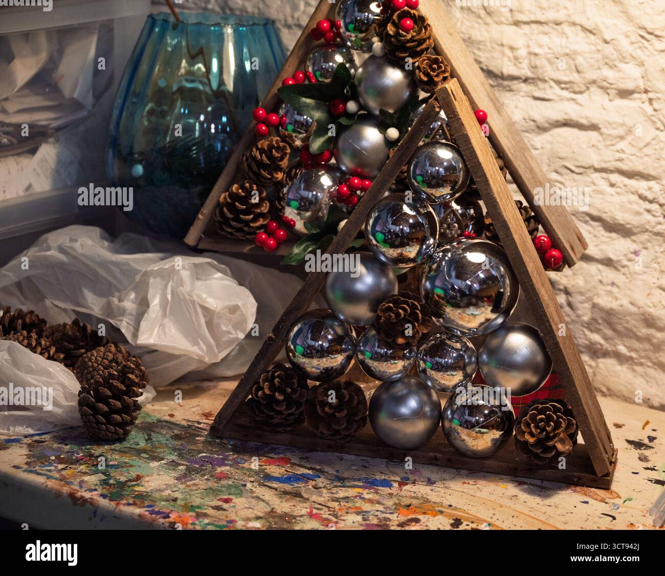 Ein Kunsthandwerker ziert einen Holzbaum mit Ornamenten, Tannenzapfen und Beeren für eine festliche Feiertagsvorstellung. Stockfoto