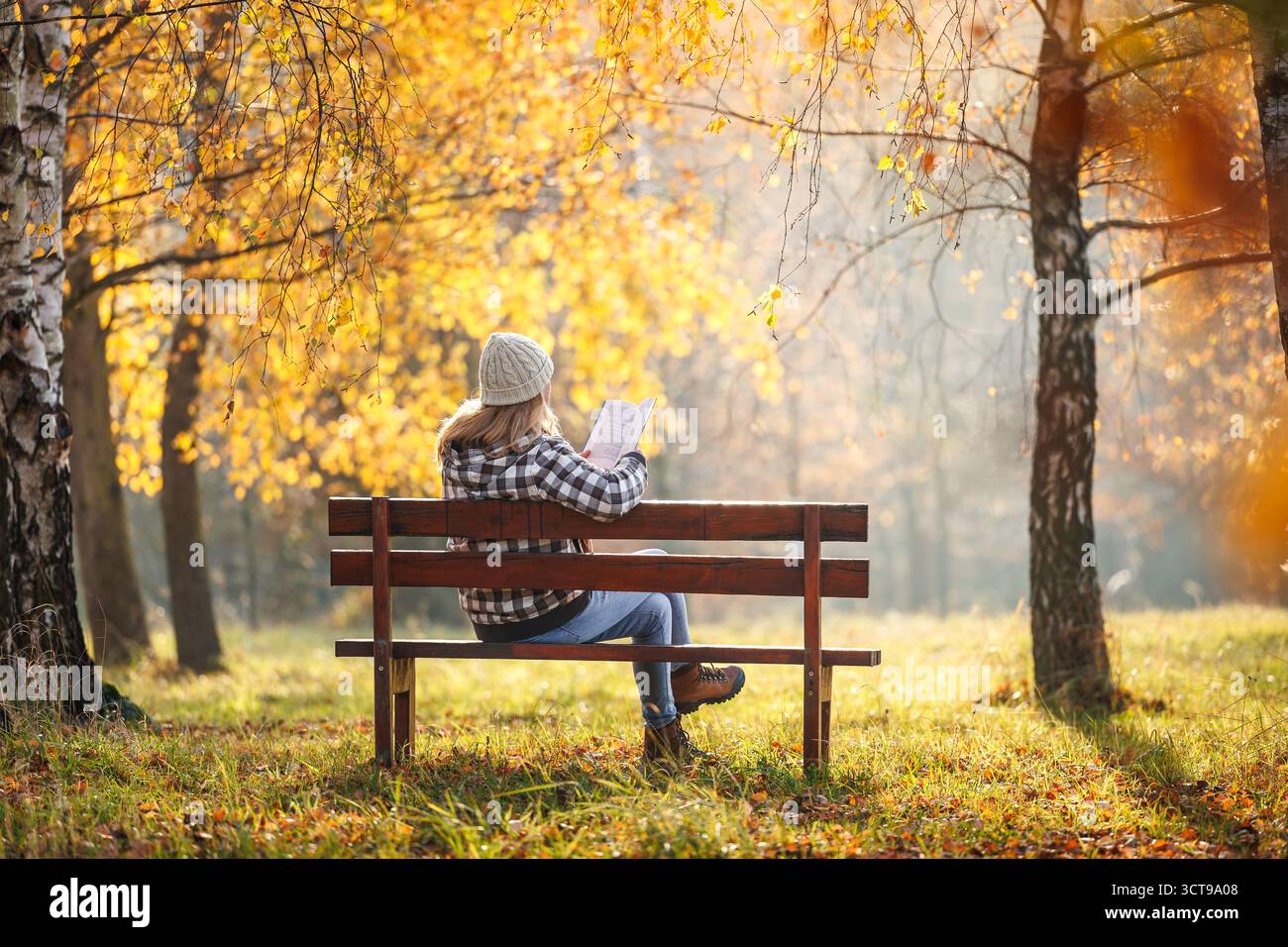 Frau liest Buch im Herbstpark. Digitale Entgiftung, geistiges Wohlbefinden und Entspannung an der frischen Luft im Freien Stockfoto