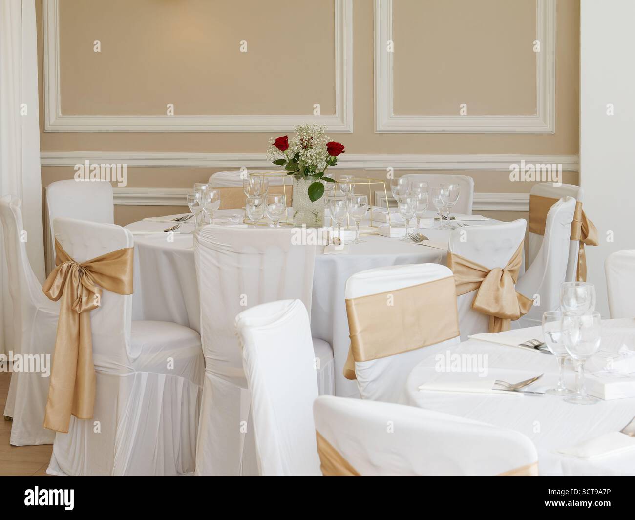 Eleganter Hochzeitstisch mit weißen Stühlen und goldenen Details in der Empfangshalle. Stockfoto