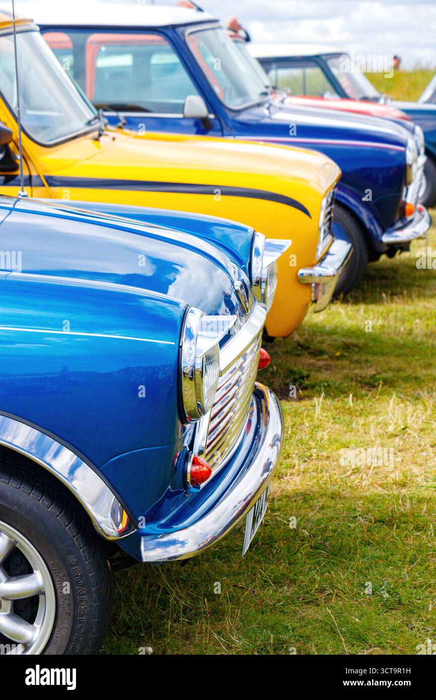 Vorderansicht einer Reihe von Vintage-Miniautos in leuchtenden Farben, die auf Rasen geparkt sind und das klassische Automobildesign aus dem Blyth Beach aus der Mitte des 20. Jahrhunderts zeigen Stockfoto