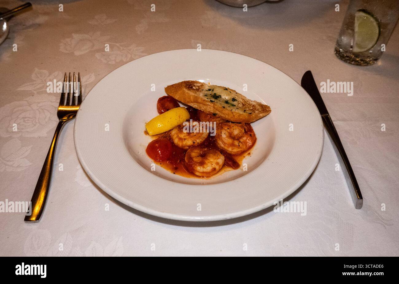 Ein köstlicher Teller Knoblauchbutter Garnelen mit geblasenen Tomaten, einem Zitronenkeil und einer Seite geröstetem Knoblauchbrot, elegant präsentiert für einen gourm Stockfoto