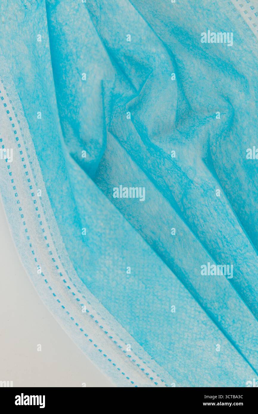 Eine medizinische Maske aus blauem Stoff liegt auf einer weißen Oberfläche und unterstreicht die weiche Textur und das mehrschichtige Design. Die Maske ist bereit für den Einsatz in einem Gesundheitswagen Stockfoto