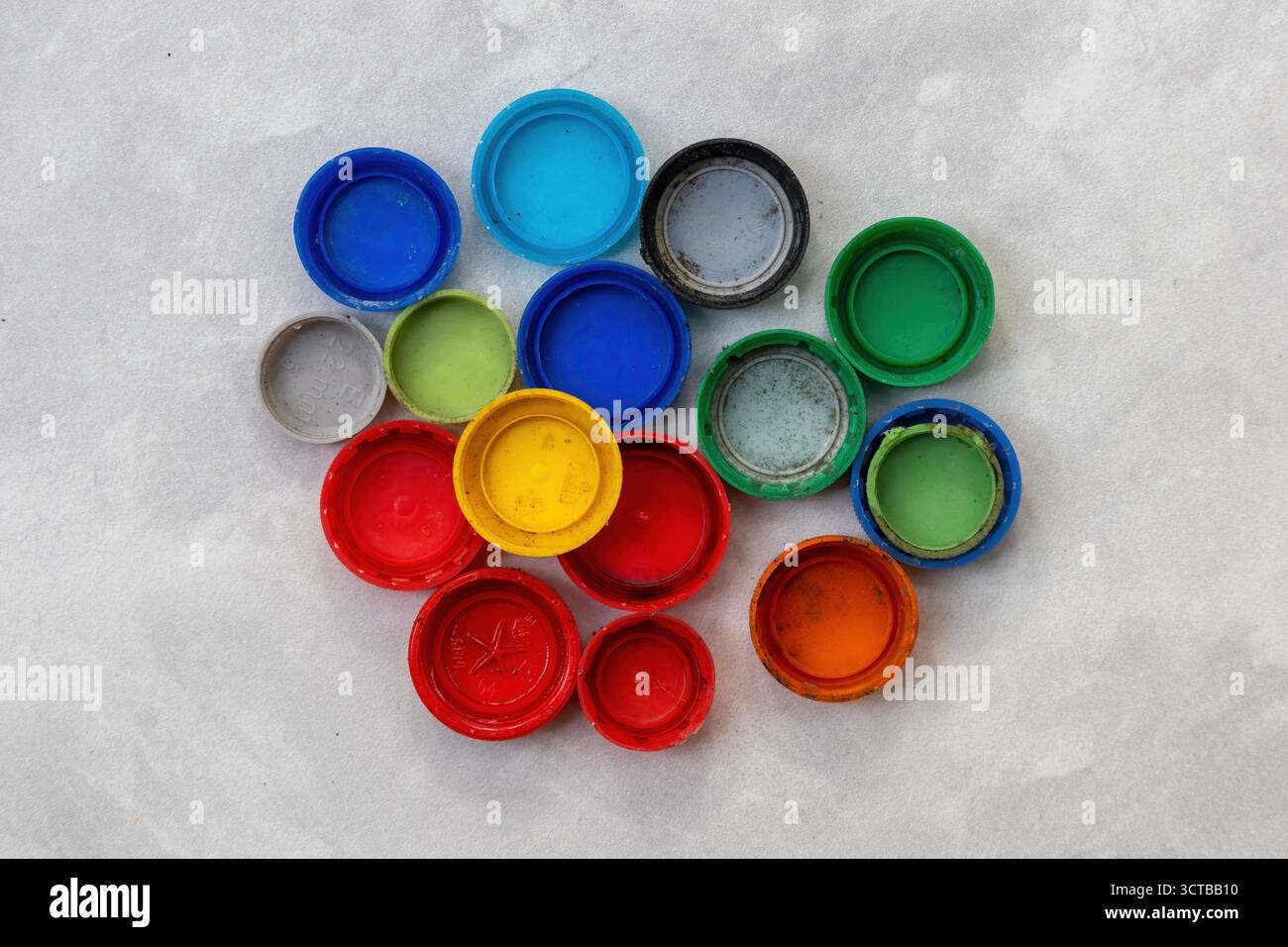 Lebhafter Haufen alter, schmutziger Plastikflaschenverschlüsse auf weißen Fliesen verteilt. Müll für Null Abfall, Verschmutzung, Nachhaltigkeit, Handwerksprojekte und Kinder Stockfoto