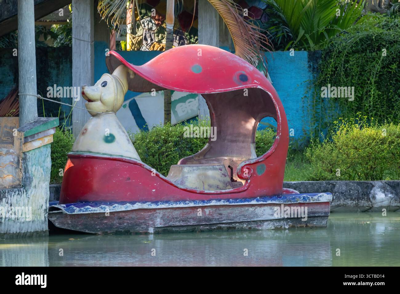 Leeres farbenfrohes Paddelboot, das an einer Dockstange in einem Vergnügungspark-Teich in Bangladesch befestigt ist. Freizeit, Sommerspaß und ruhige Wassersportangebote Stockfoto