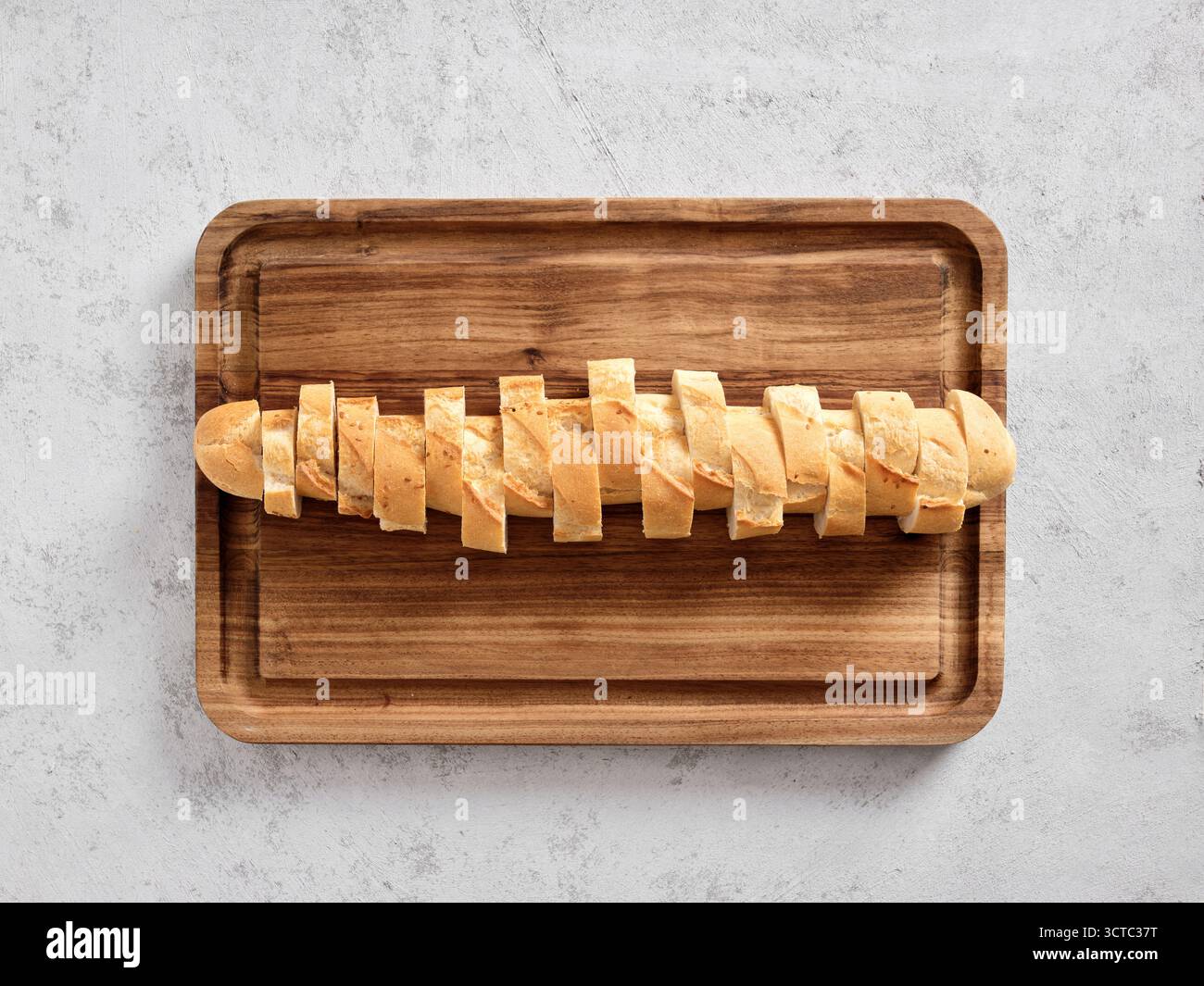 In Stücke geschnittenes Baguette-Brot auf einem rechteckigen Holzschneidebrett. Zubereitung frischer Vorspeisen oder einer Mahlzeit Stockfoto