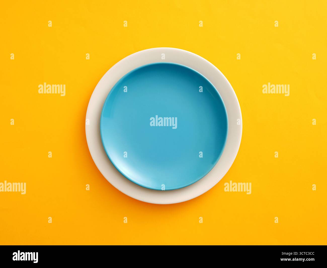 Leere blaue Platte auf einer weißen Tafel, die einen starken Kontrast von komplementären Farben, Konzept von Essen, Küchenutensilien und Design schafft. Modell für das Platzieren von Lebensmitteln oder Stockfoto