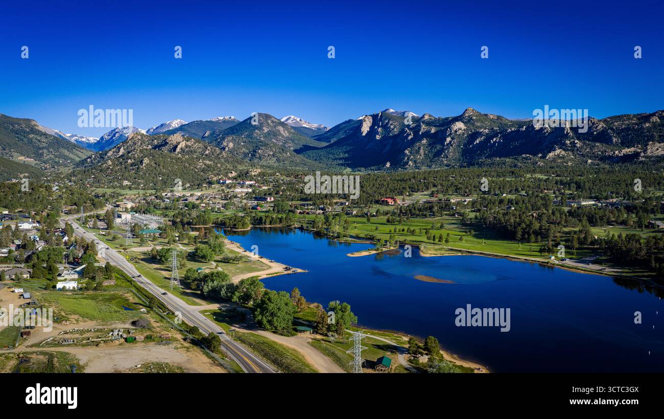 Aus der Vogelperspektive auf den ruhigen Lake Estes, der den leuchtend blauen Himmel reflektiert, eingebettet zwischen üppigem Grün und zerklüfteten Berggipfeln, Estes Park, Colorado, USA. Stockfoto