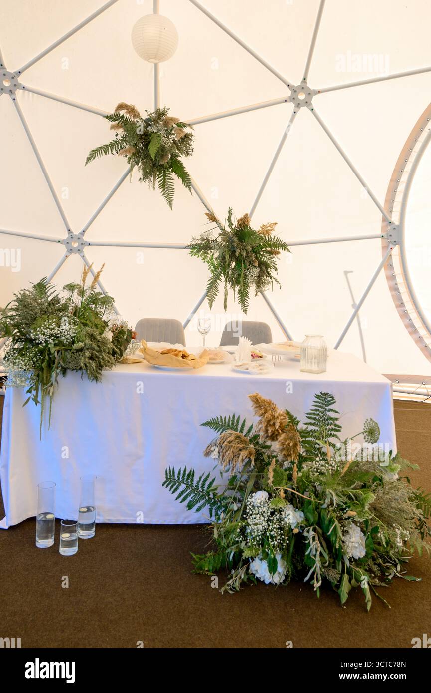 Hochzeitstisch mit natürlichen Pflanzen und getrockneten Blumen in einem weißen Zelt. Ein Hochzeitstisch mit umweltfreundlichem Dekor aus Grün und Farnen Stockfoto