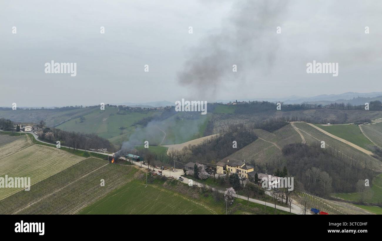 Aus der Vogelperspektive brennende Traubenzweige und Rauch, der über den malerischen sanften Hügeln von Piacenza Italien aufsteigt, eine ländliche Landschaft während der landwirtschaftlichen Clea Stockfoto