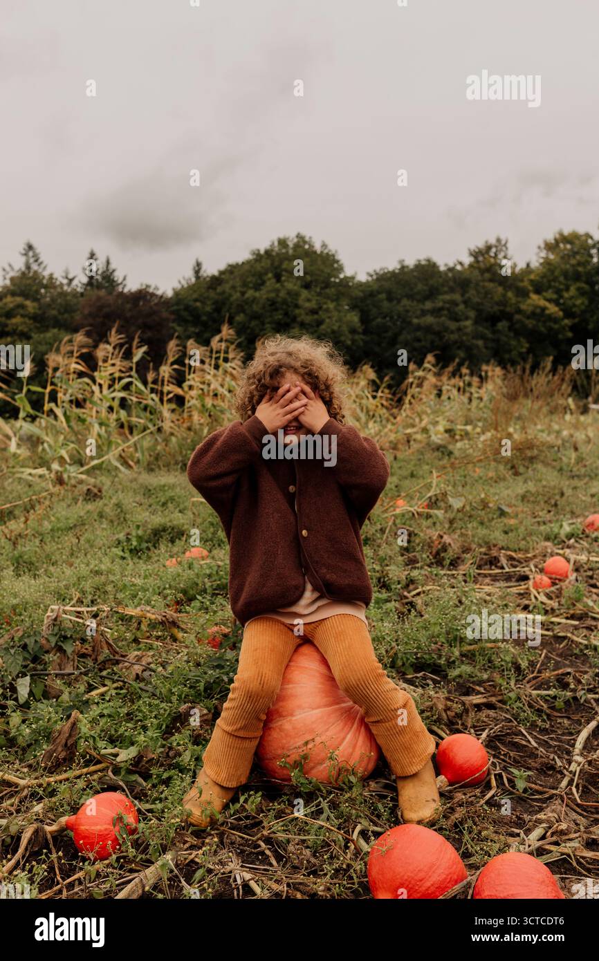 Kind, das auf Kürbis auf einem Herbstfeld sitzt Stockfoto