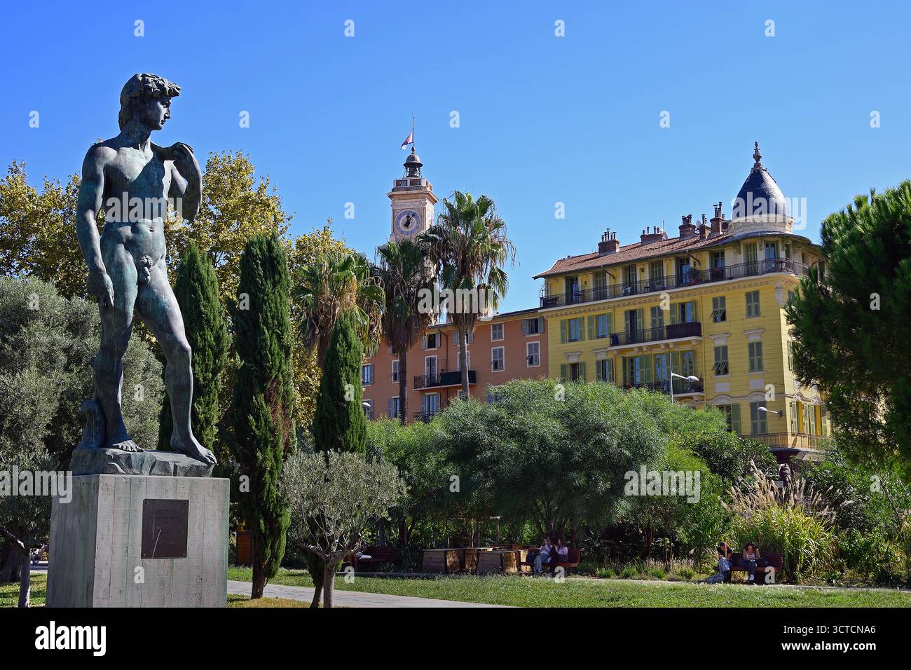 Bronze-Nachbildung von Michelangelos David-Skulptur auf der Promenade du Paillon (Coulée Verte) mit dem Saint-Francois-Uhrenturm und farbenfrohen Gebäuden Stockfoto