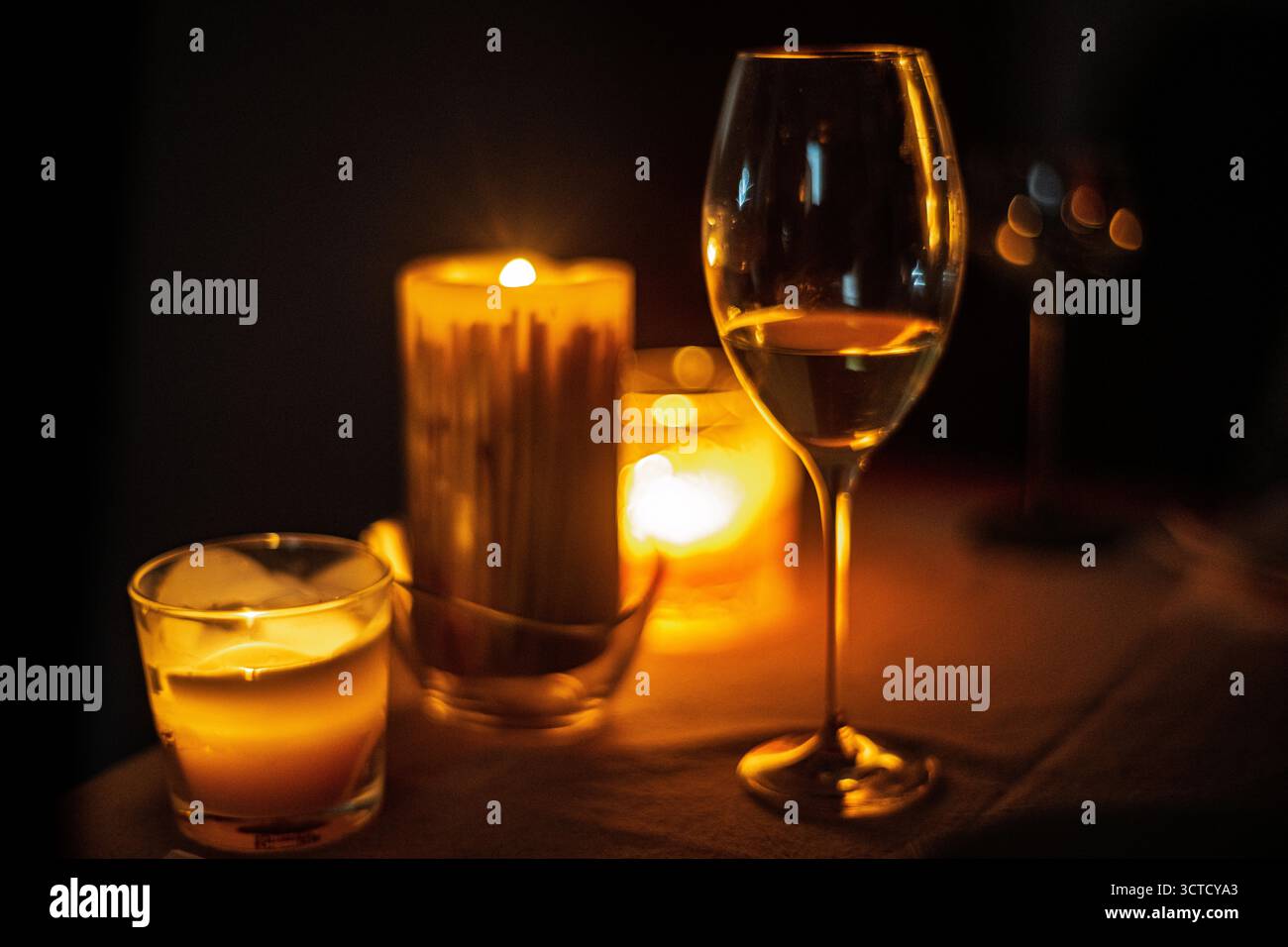 Der Weißwein leuchtet bei Kerzenlicht sanft und schafft eine beruhigende Atmosphäre. Die Schatten unterstreichen die intime Umgebung und laden zur Entspannung und Ruhe ein Stockfoto