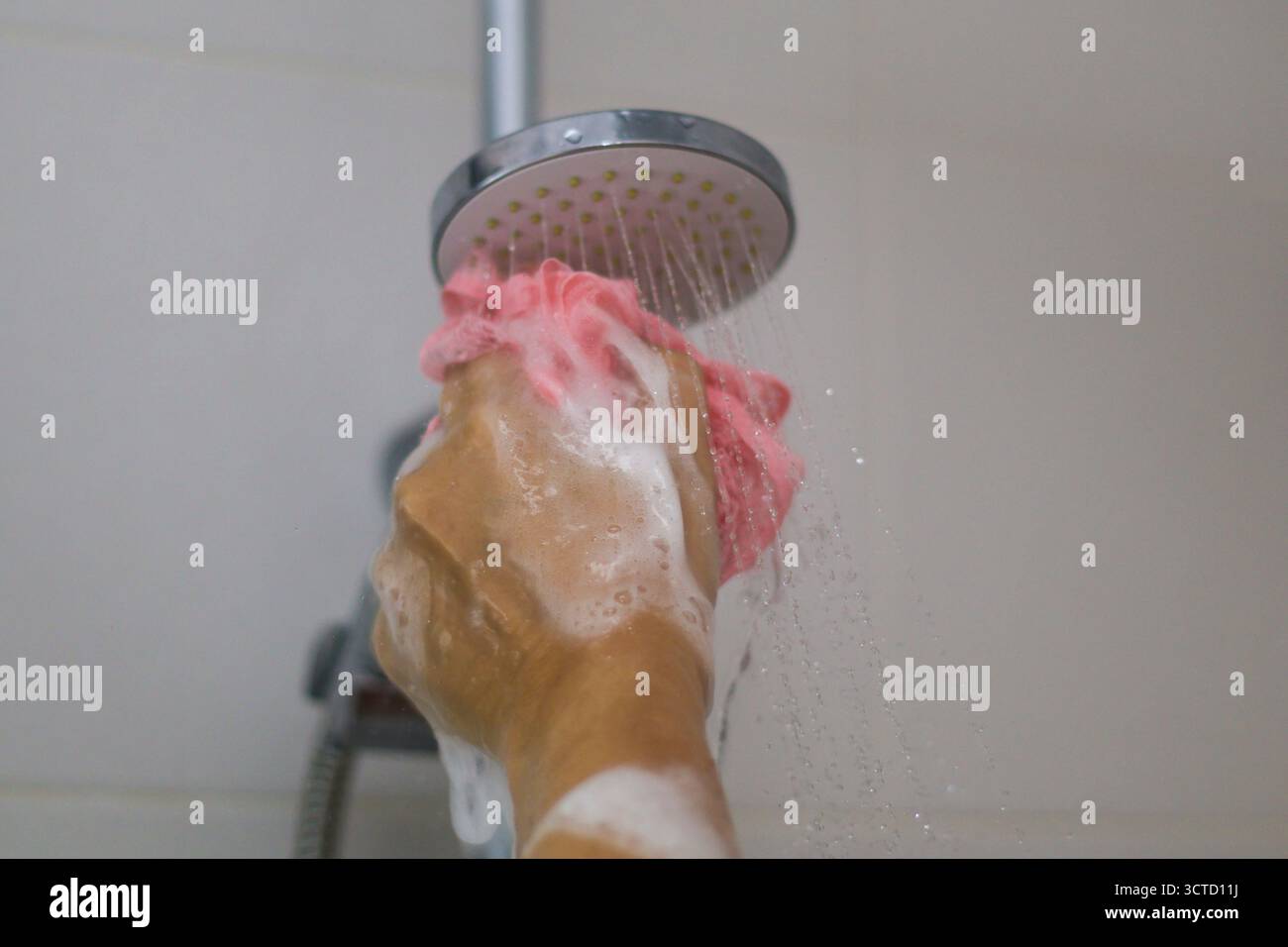 Die Hand der Person unter strömendem Wasser hält einen rosa Schwamm mit weißer Seifenlauge während einer erfrischenden Dusche Stockfoto
